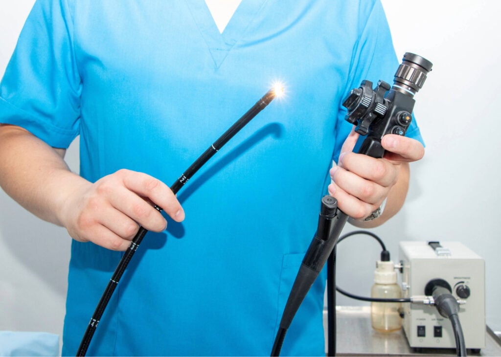 Medical professional holding an upper GI endoscopy scope with a lighted tip, demonstrating its components against a clinical background.