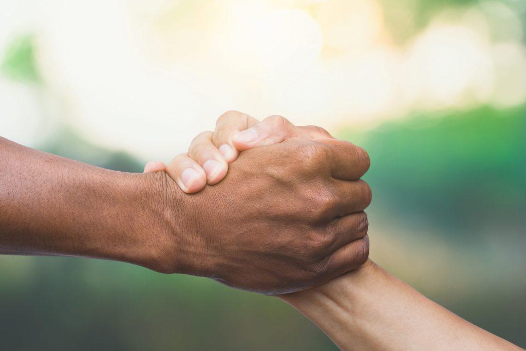 Two people clasp hands firmly in a handshake against a blurred outdoor background, symbolizing trust and reassurance before a colonoscopy.