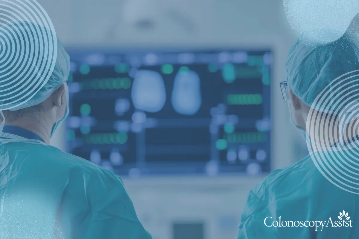 Two medical professionals in scrubs and caps observe a monitor displaying medical images and data, with the text Colonoscopy Assist in the bottom corner.