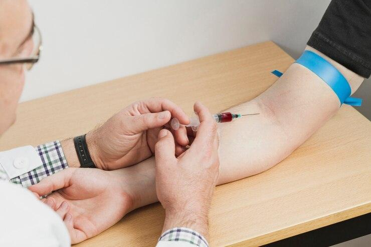 A healthcare professional from ColoHealth expertly draws blood from a persons arm using a syringe, securing it with a blue tourniquet for precision.