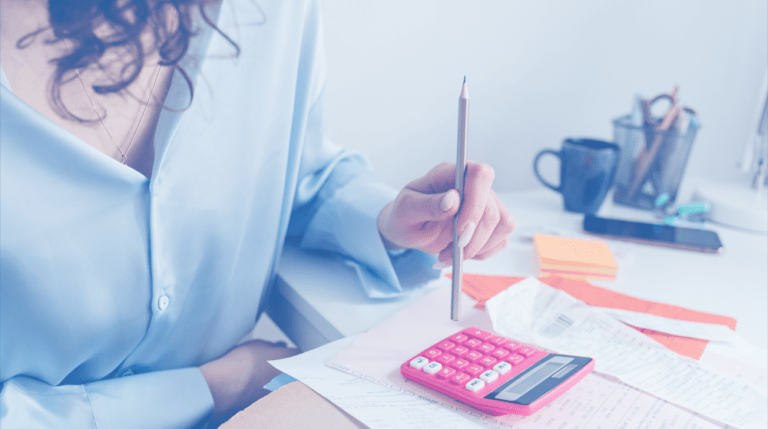 A person in a blue shirt uses a pink calculator and holds a pencil over paperwork related to arranging a low-cost colonoscopy at a desk.