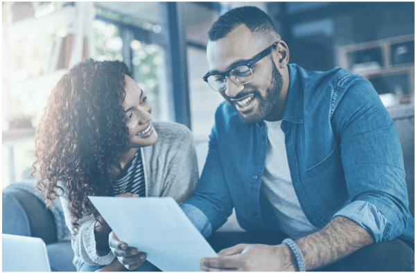 A smiling couple looks over a document about low-cost colonoscopy options while sitting on a couch in a bright room.