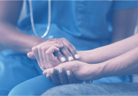 A healthcare professional in blue scrubs gently holds the hands of another person, offering comfort and support before a colonoscopy.